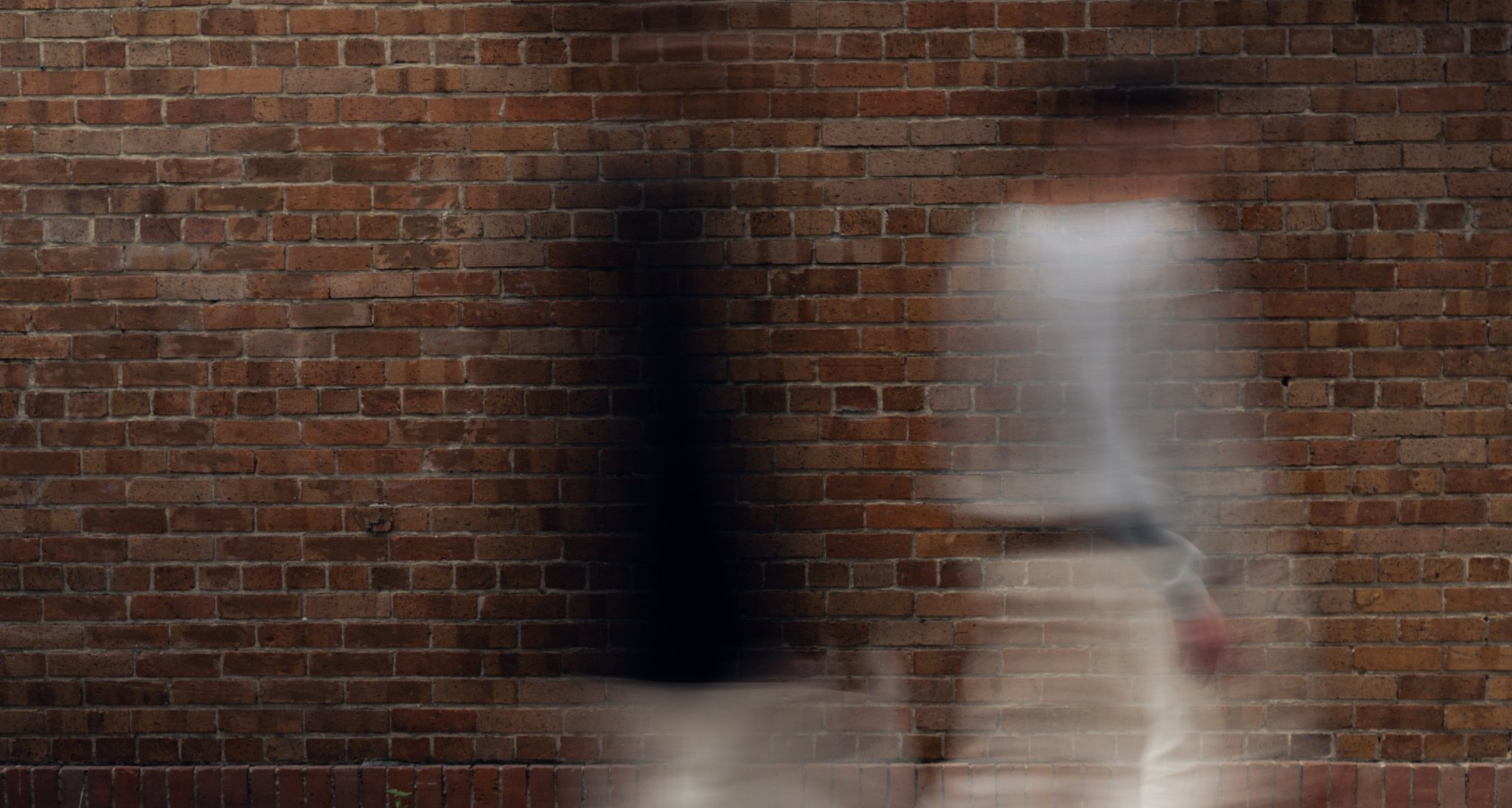 A figure in motion streaks past a brick wall, blurred by a long shutter