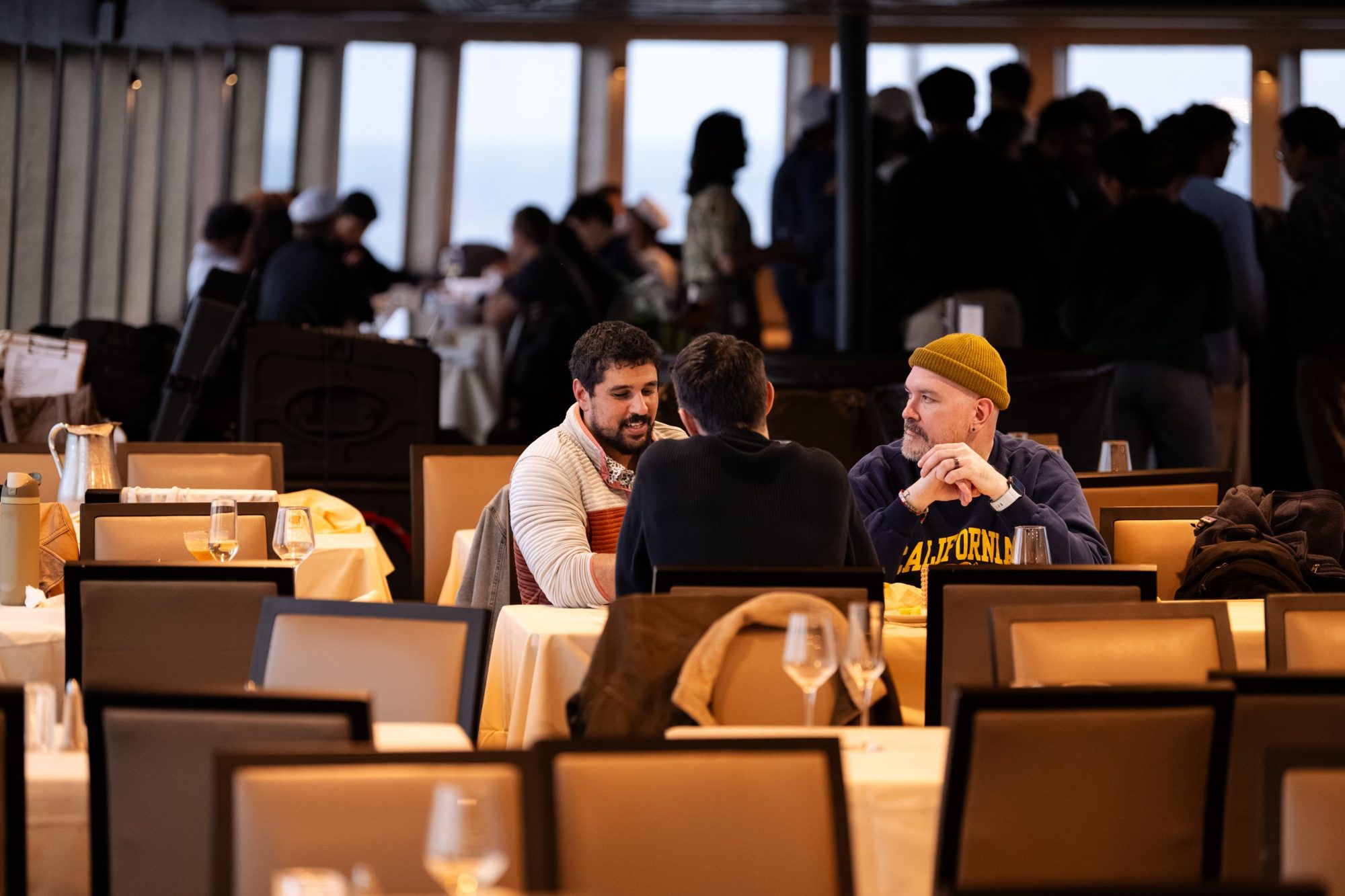 Tony in a mustard beanie and California sweatshirt, talking with two product people at a table during a Distyl event