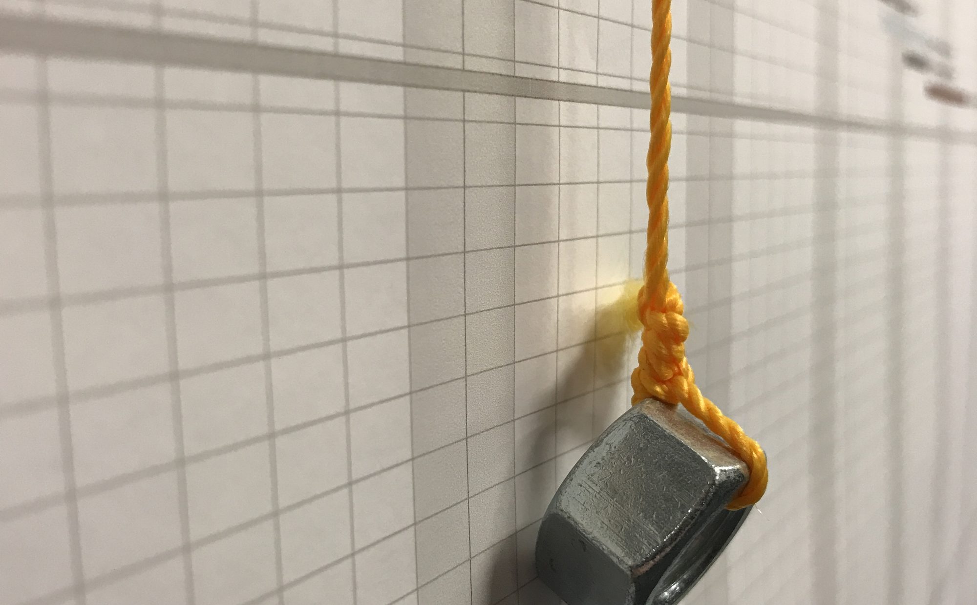 A steel nut on orange string hanging against a printed project schedule taped to a wall