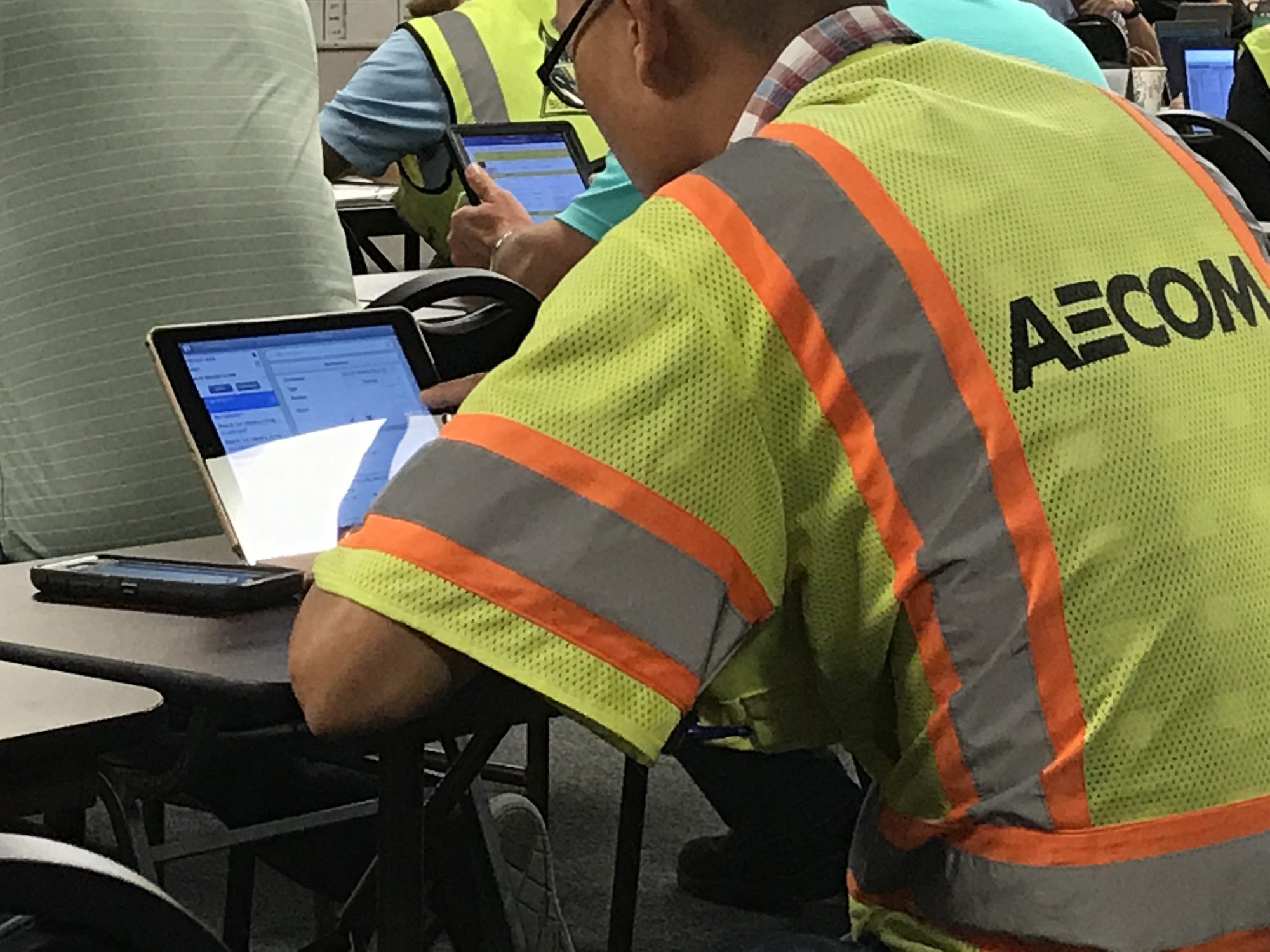 A worker in a high-visibility vest using a laptop at a folding table