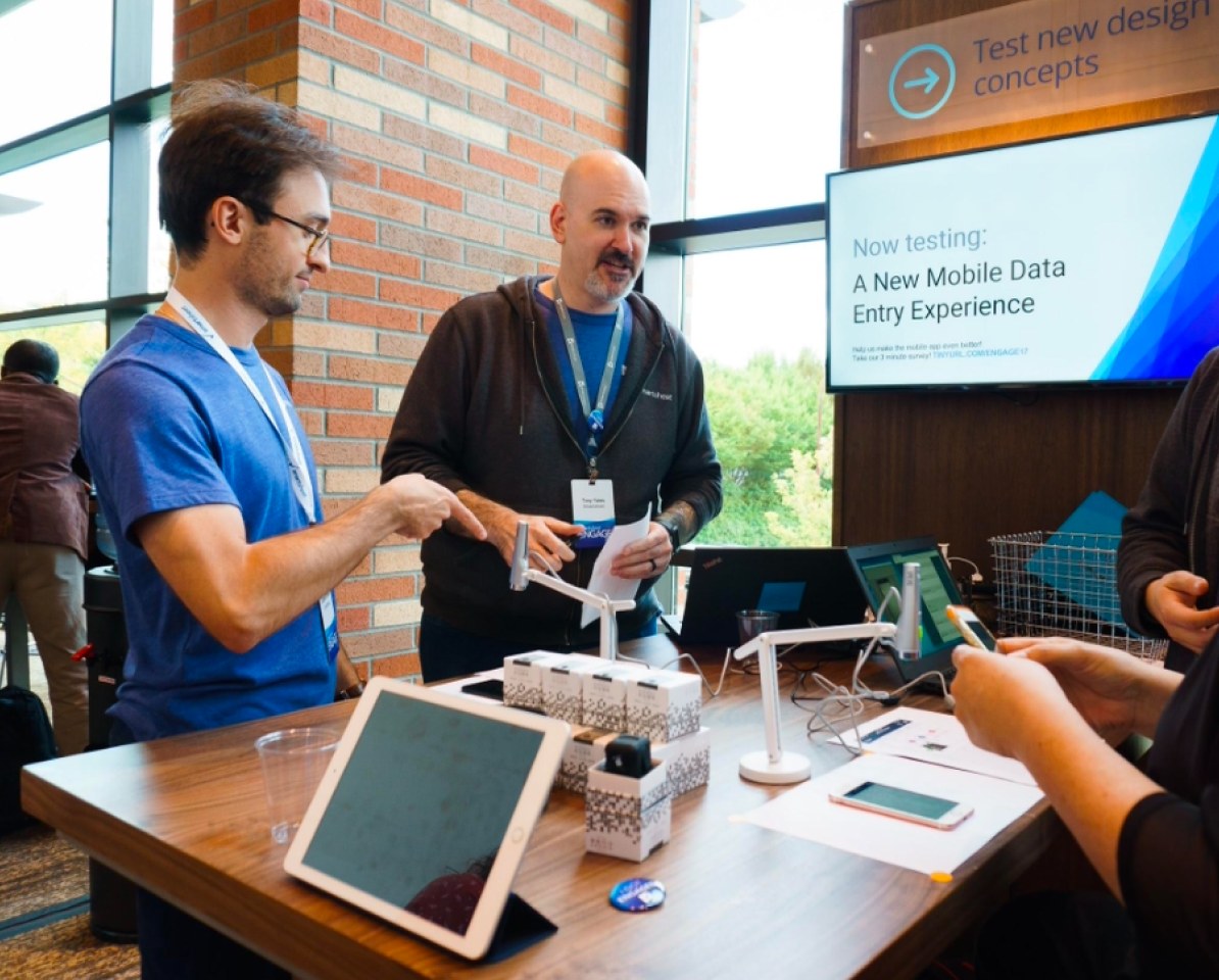 Tony at the Engage 2017 test-new-design-concepts booth, talking with a customer next to a screen reading Now testing: A New Mobile Data Entry Experience