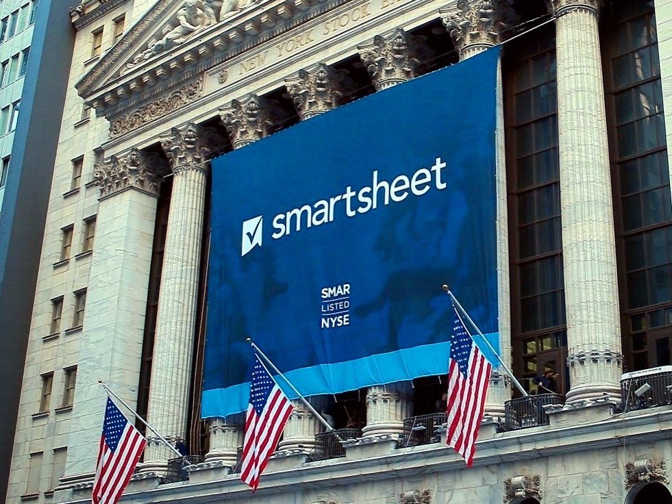 A Smartsheet banner reading SMAR Listed NYSE hanging across the columns of the New York Stock Exchange