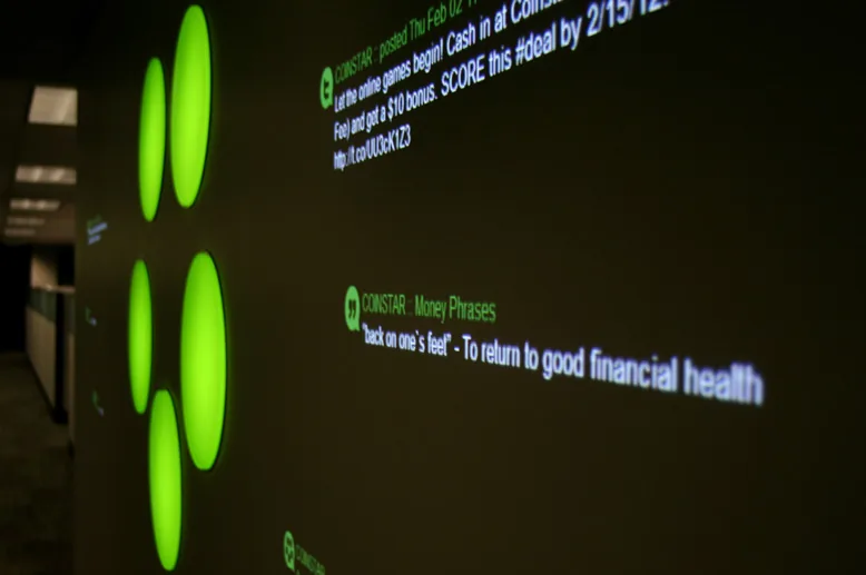 Coinstar office wall with glowing green logo dots and projected social posts