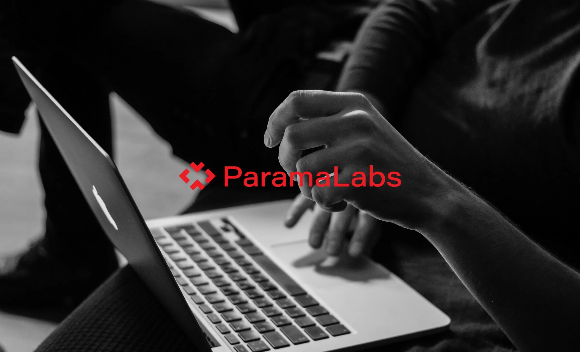 Red ParamaLabs logo over a black and white photo of hands at a laptop