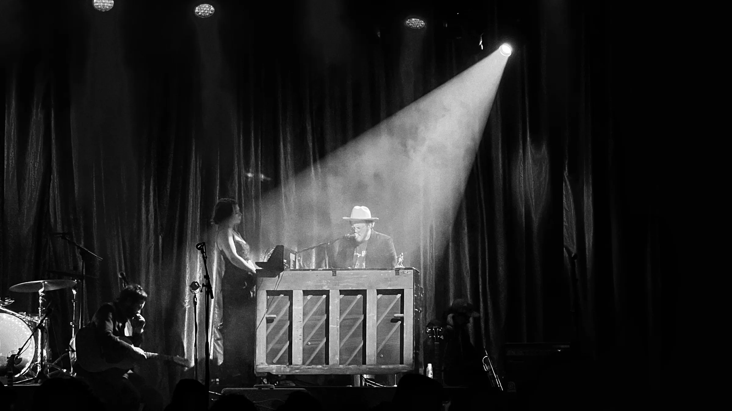 Black and white concert photo of a singer at an upright piano under a single spotlight
